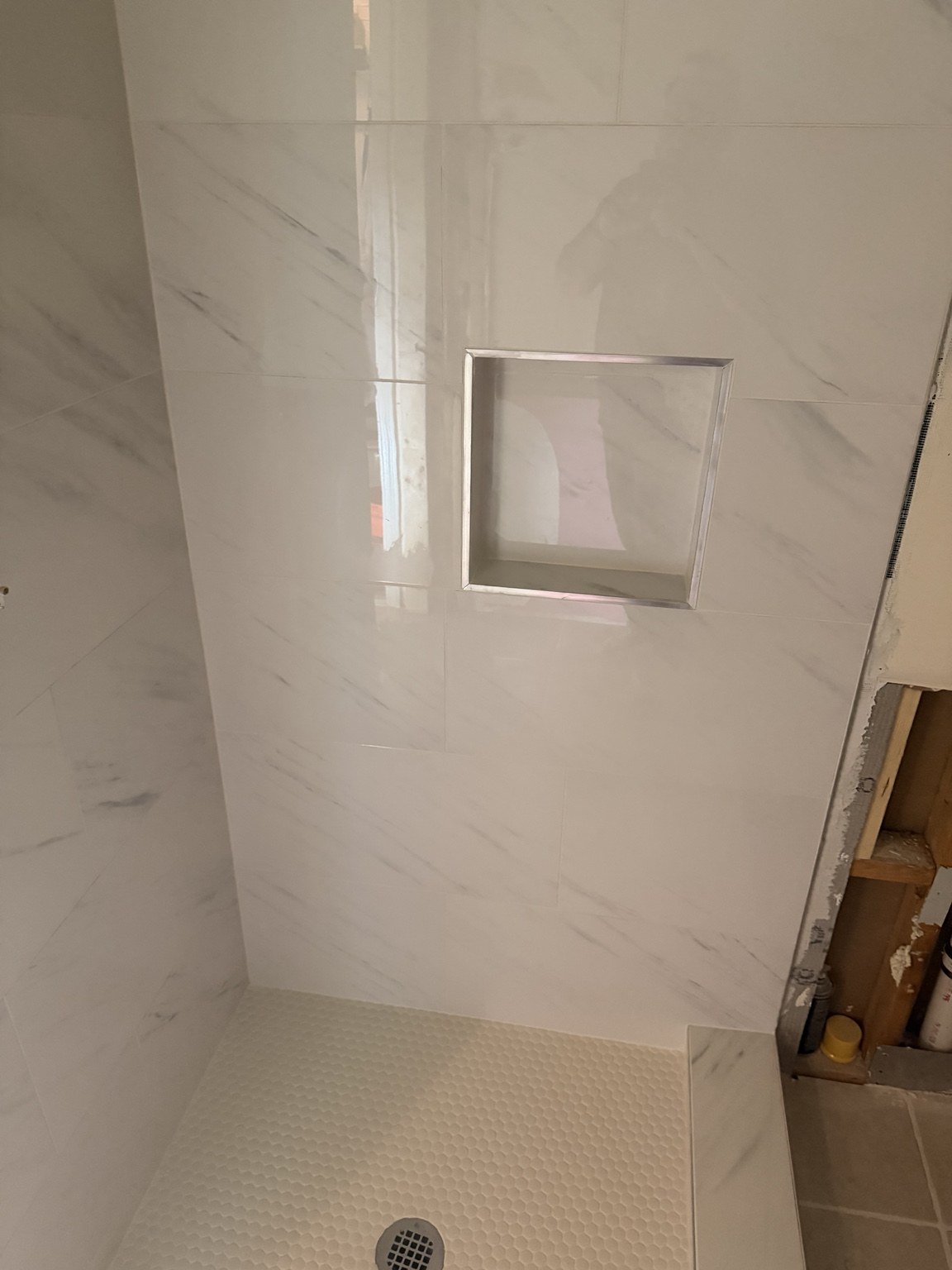 Light marble-look shower wall with recessed niche and mosaic floor