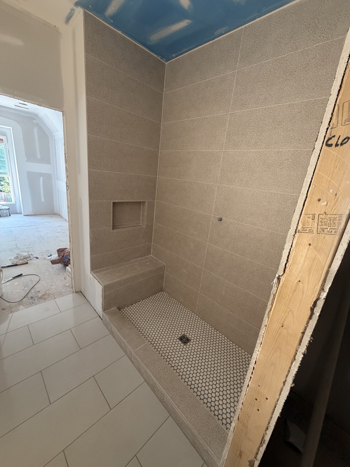 Large-format gray shower tile with a niche and mosaic shower floor, during installation