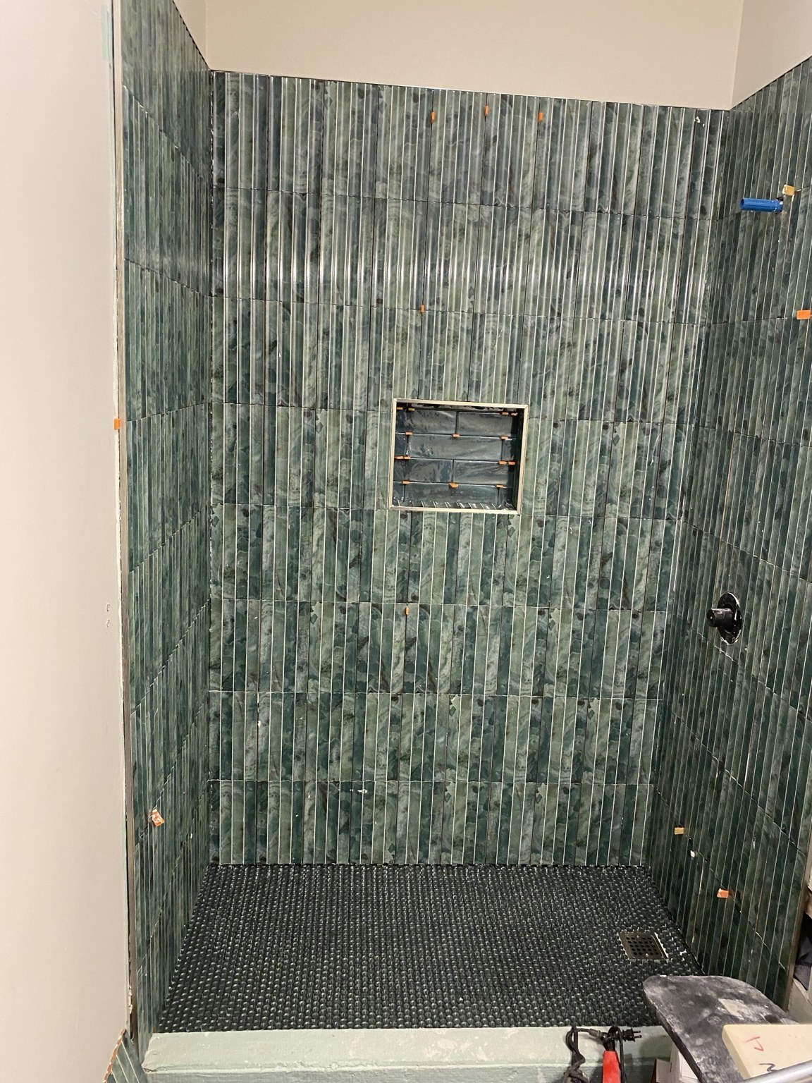 Green mosaic shower tile with a built-in niche and dark mosaic floor