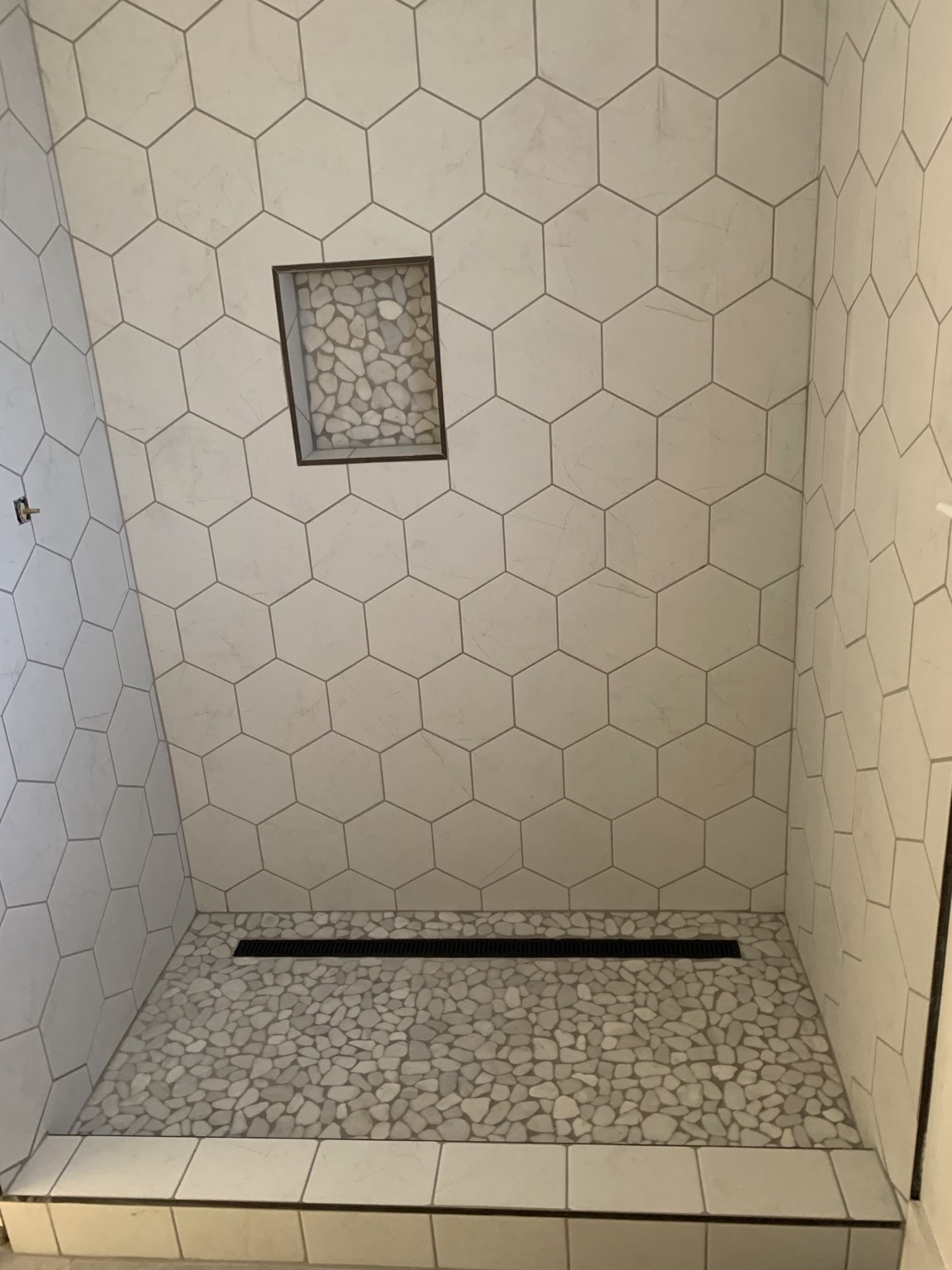 Hexagonal shower wall tile with pebble mosaic niche and floor and linear drain