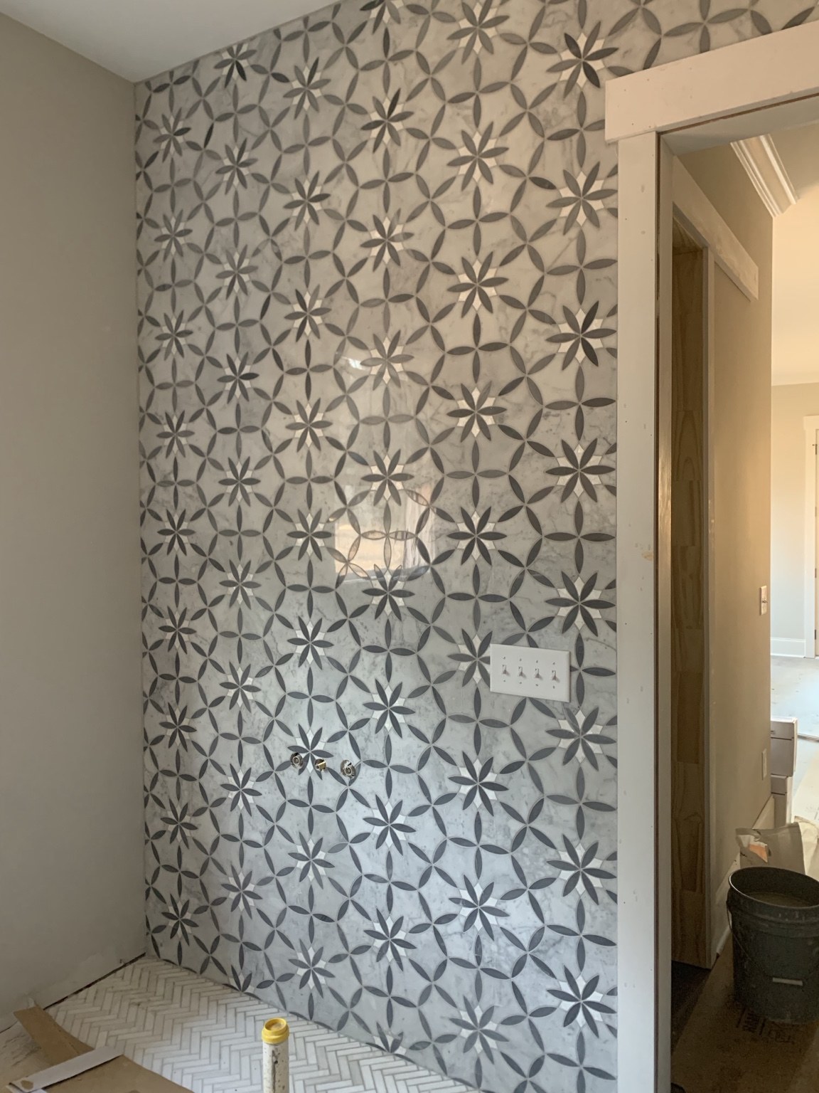 Floral-pattern bathroom accent wall with herringbone floor tile during installation