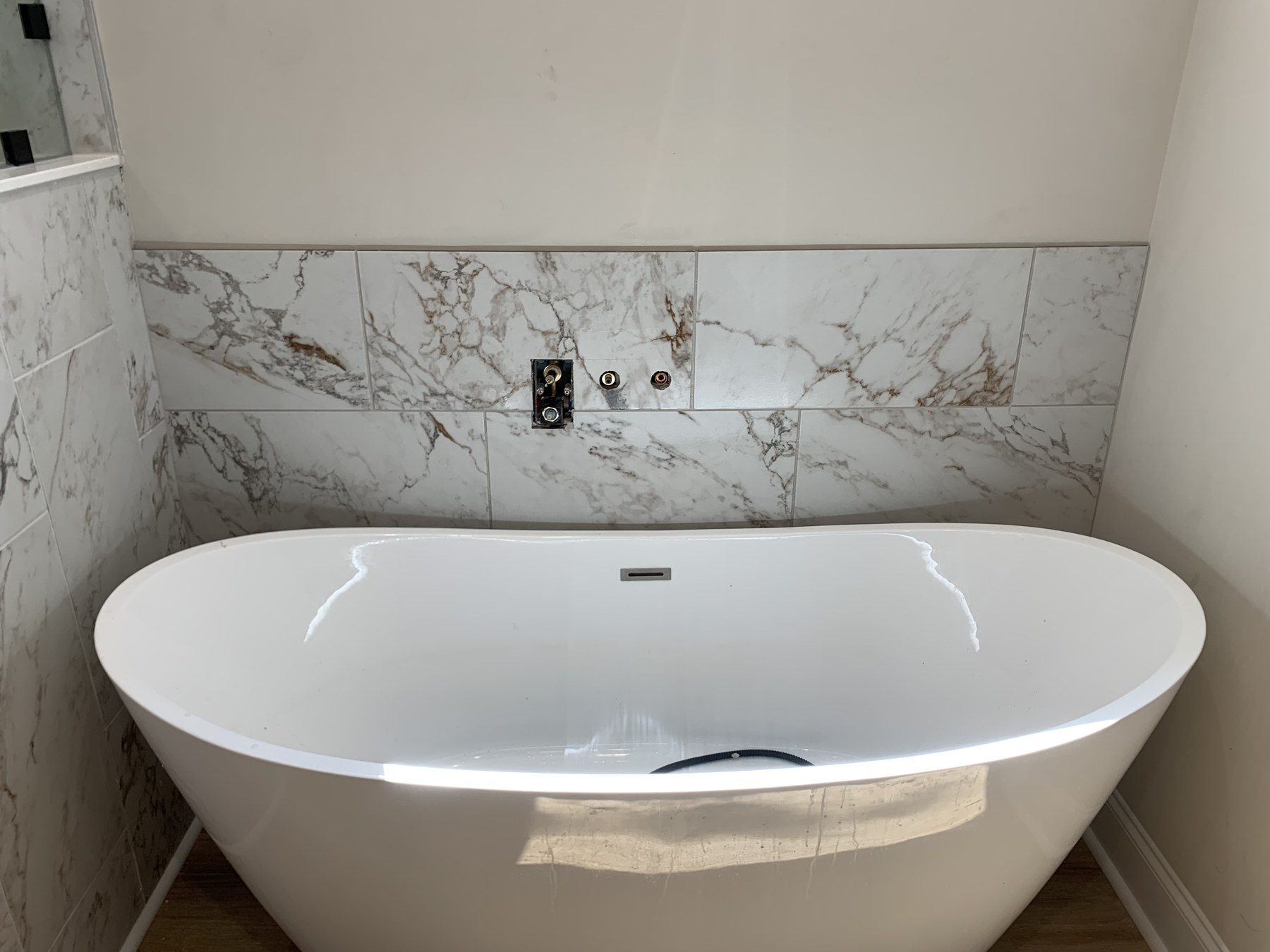 Freestanding bathtub surrounded by large marble-look wall tiles during installation