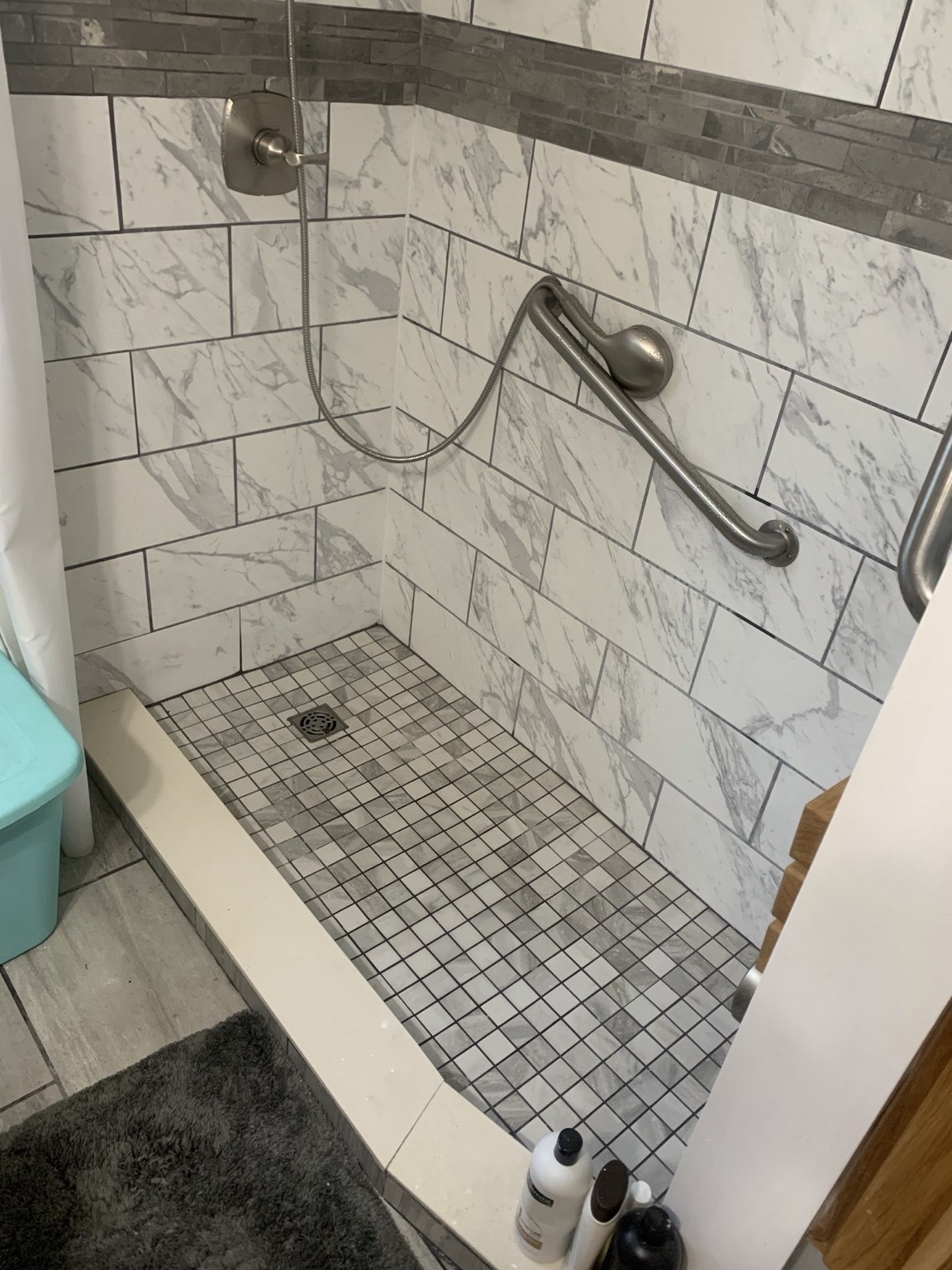 Marble-look tiled shower with gray accent band, grab bars and mosaic floor