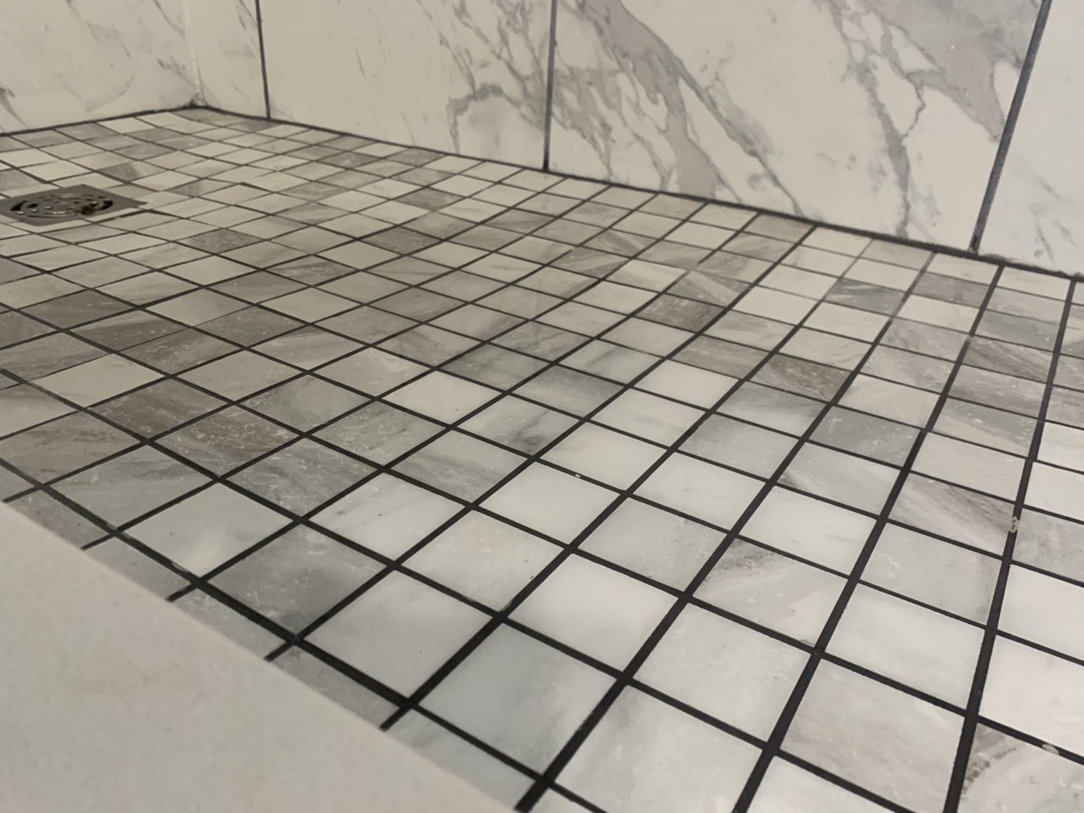 Close-up of gray and white square mosaic shower floor with dark grout